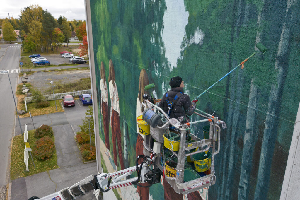 Eloise Gillow painting a mural on the wall of a 9 storey high block of flats