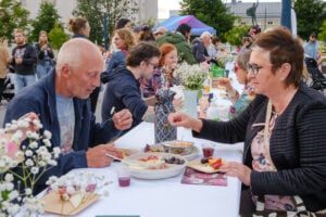 People sitting down at the Long Table Dinner in August 2023. Ihmisiä ruokailemassa ulkona 2023 järjestetyssä Kesäillan kattauksessa.