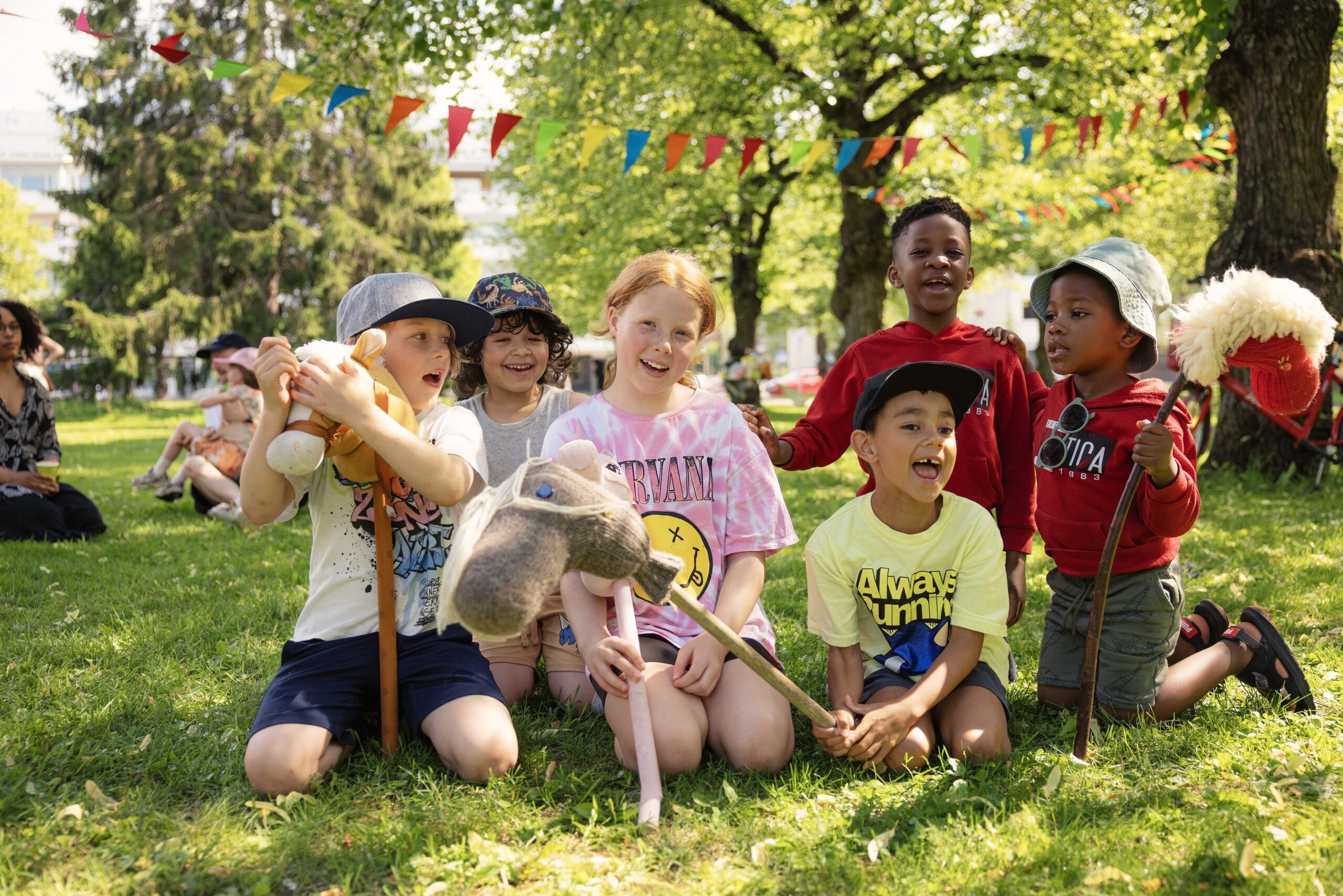 Lapset leikkivät keppihevosilla puistossa.