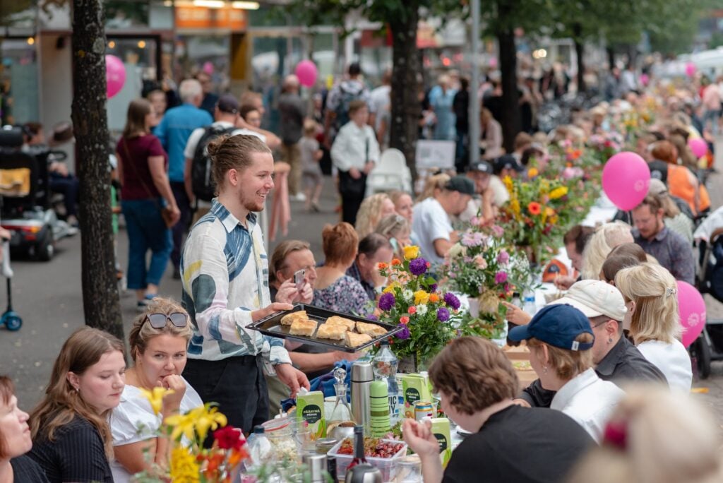 Ulkoilmajuhla, ihmisiä syömässä pitkän pöydän ääressä.