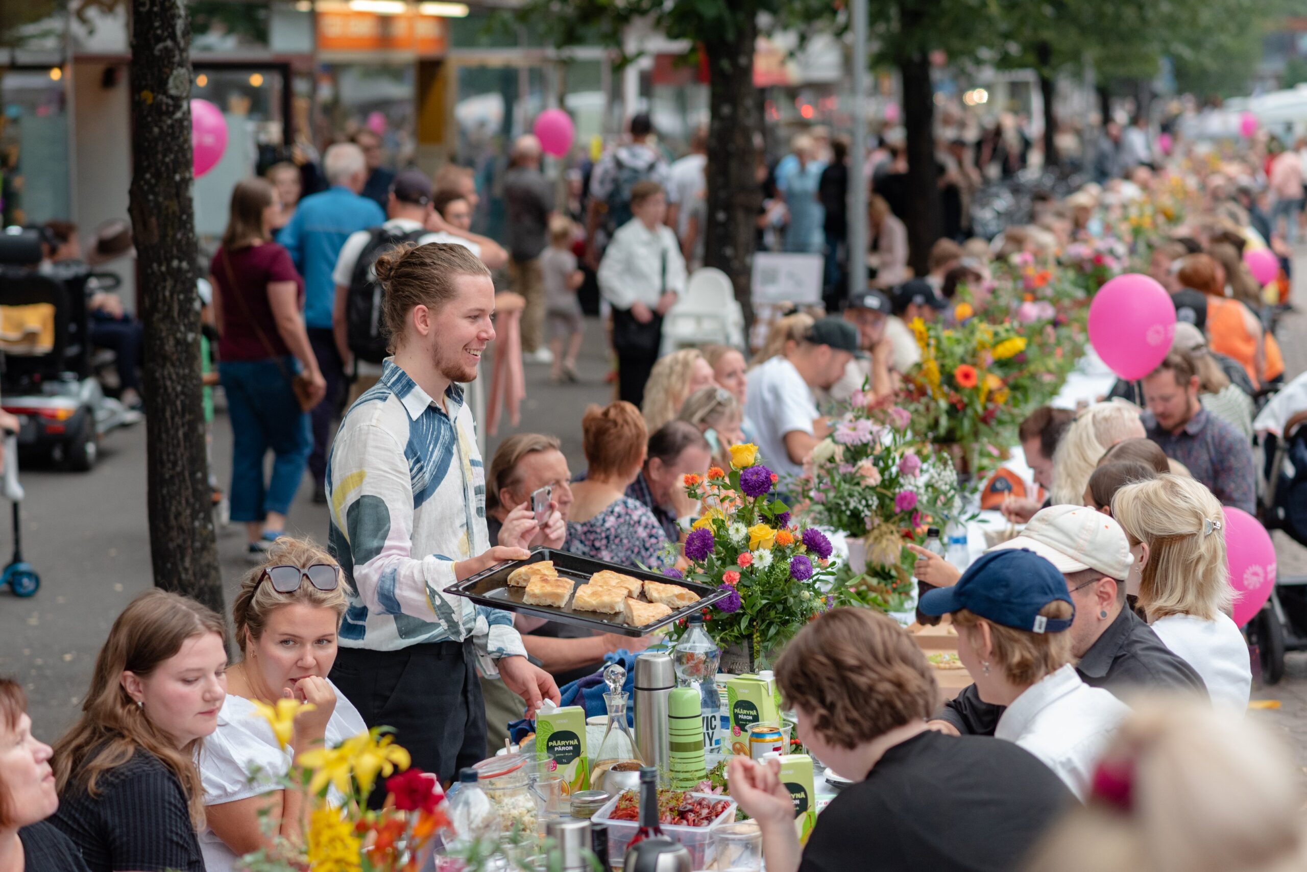 Ulkoilmajuhla, ihmisiä syömässä pitkän pöydän ääressä.