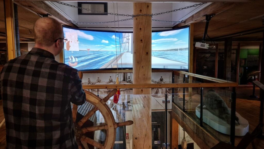 Museokävijä ohjaa purjelaivaa Raahen redille Kotiväylällä -pelissä oikeaa ruoria käyttäen. Kuva: Anna Latomaa/Raahen museo