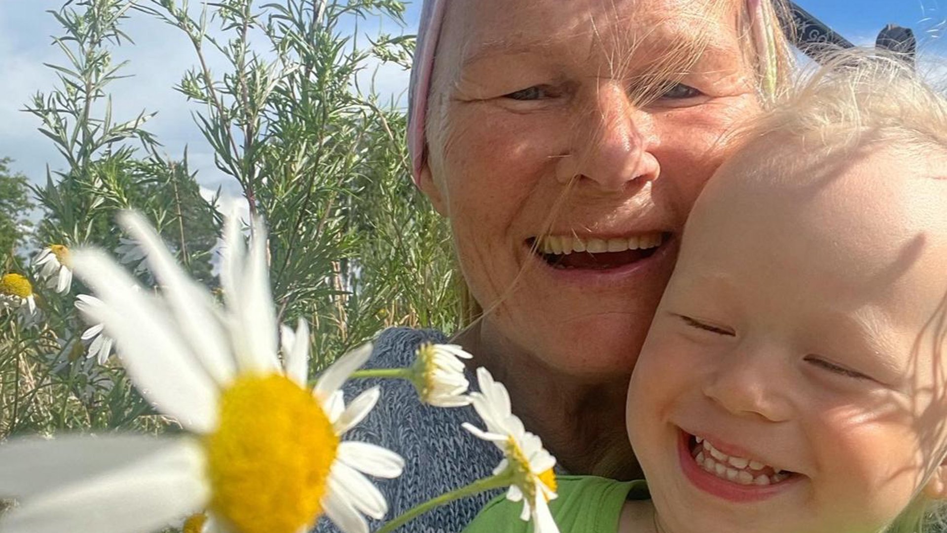 Grandmother Kaija and her grandchild share a joyful laugh together in the summer nature. Behind them, wildflowers such as cow parsley and daisies frame this moment of happiness. Photo rights: Kaija Wittenberg.