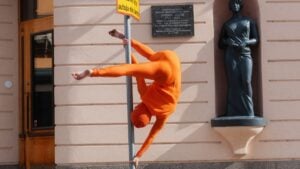Akrobaatti oranssissa puvussa tolpan ympärillä