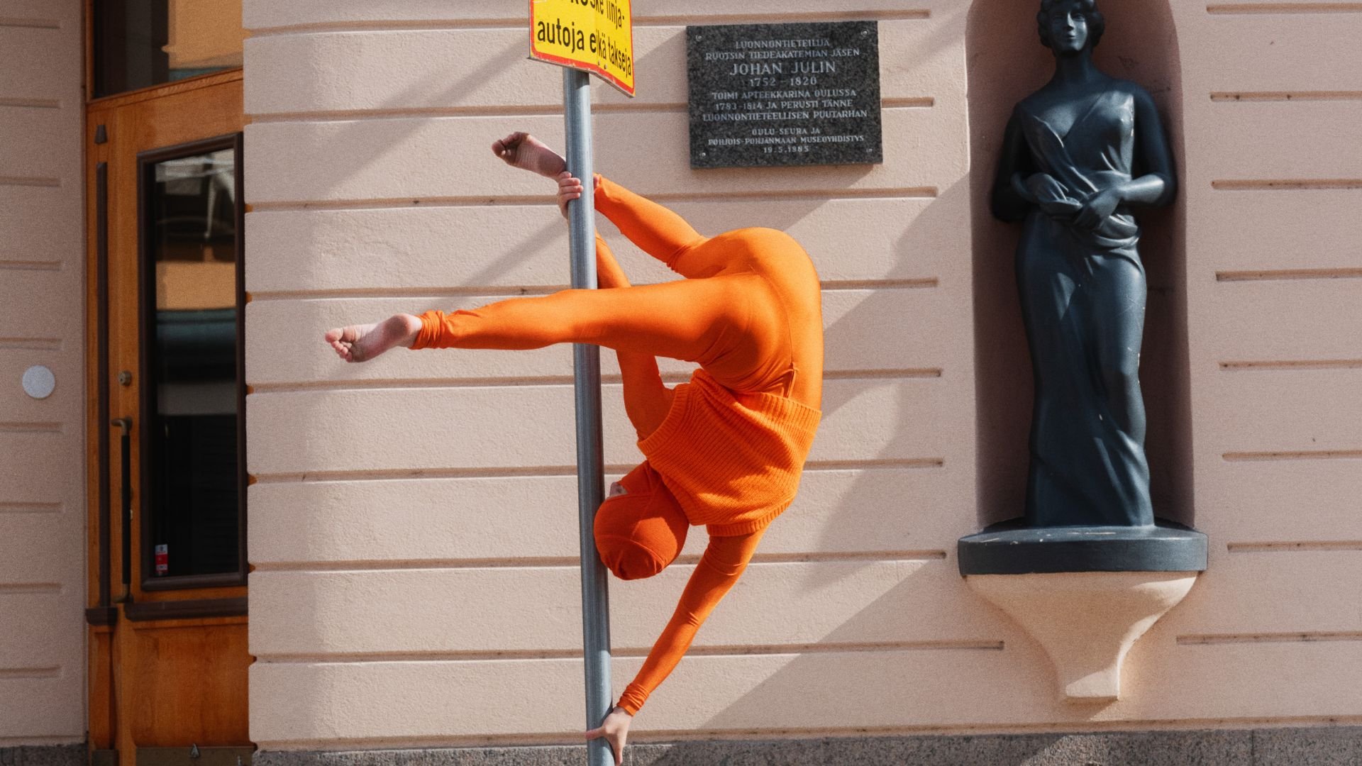 Akrobaatti oranssissa puvussa tolpan ympärillä