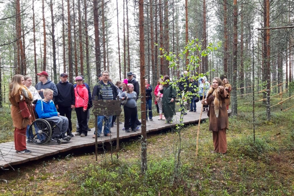 Group guided tour in forest on wooden pathway.