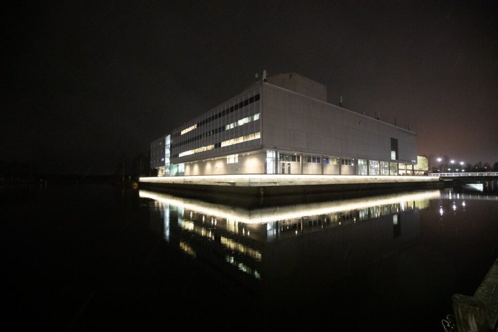 Modern building illuminated at night by riverside.