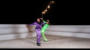 Kaksi henkilöä tanssii värikkäissä puvuissa ulkona yöllä.