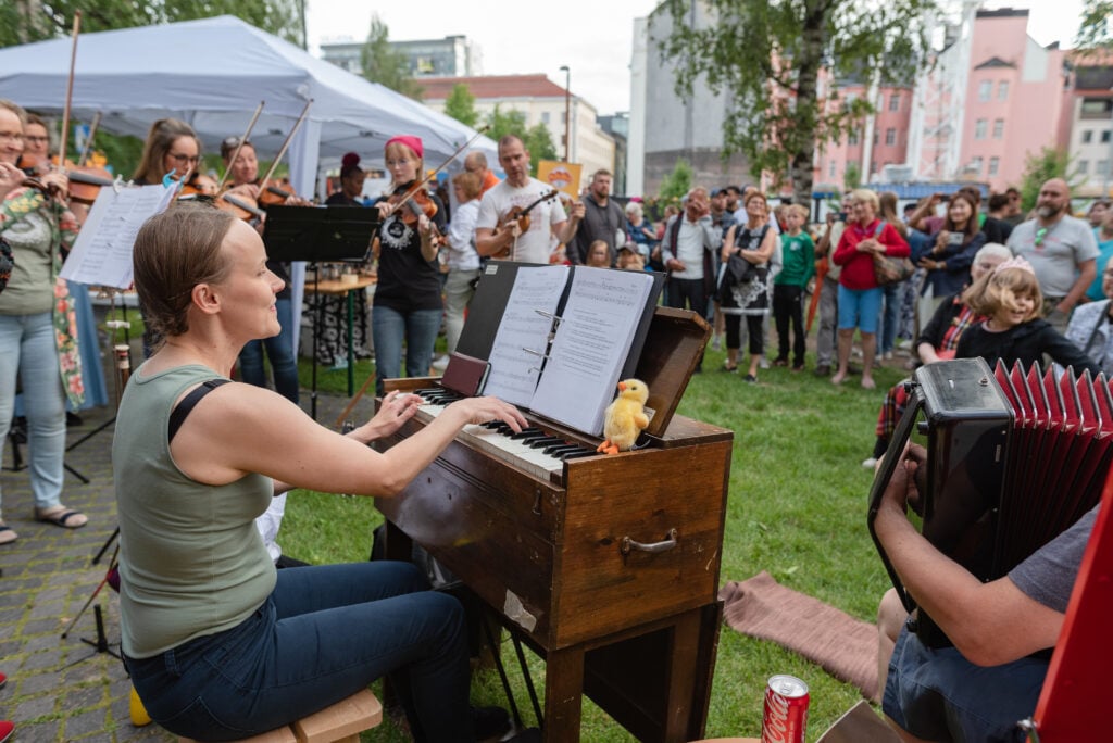 Kuvassa pelimannikollektiivi Orivesi All Stars esiintyy Kesäillan kattaus -tapahtumassa Oulun keskustassa. Ympärillä iloinen yleisö.