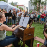 Kuvassa pelimannikollektiivi Orivesi All Stars esiintyy Kesäillan kattaus -tapahtumassa Oulun keskustassa. Ympärillä iloinen yleisö.