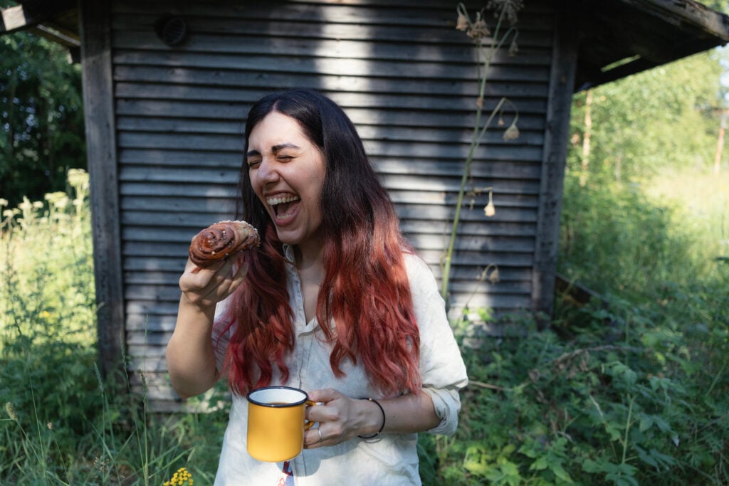 Nainen syö luonnossa kesällä korvapuustia ja juo kahvia.