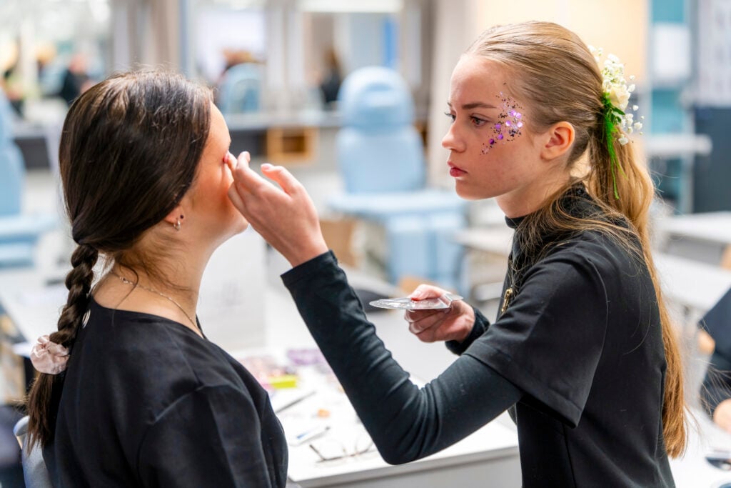 Kosmetologiopiskelijat kiinnittävät ekoglitteriä esimerkiksi silmäkulmiin ja poskipäille. He ovat miettineet, missä järjestyksessä glitter lisätään ja miten se saadaan näyttämään siistiltä kiireessäkin. Kuva: Jouni Ylisuutari / OSAO.