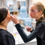 Kosmetologiopiskelijat kiinnittävät ekoglitteriä esimerkiksi silmäkulmiin ja poskipäille. He ovat miettineet, missä järjestyksessä glitter lisätään ja miten se saadaan näyttämään siistiltä kiireessäkin. Kuva: Jouni Ylisuutari / OSAO.