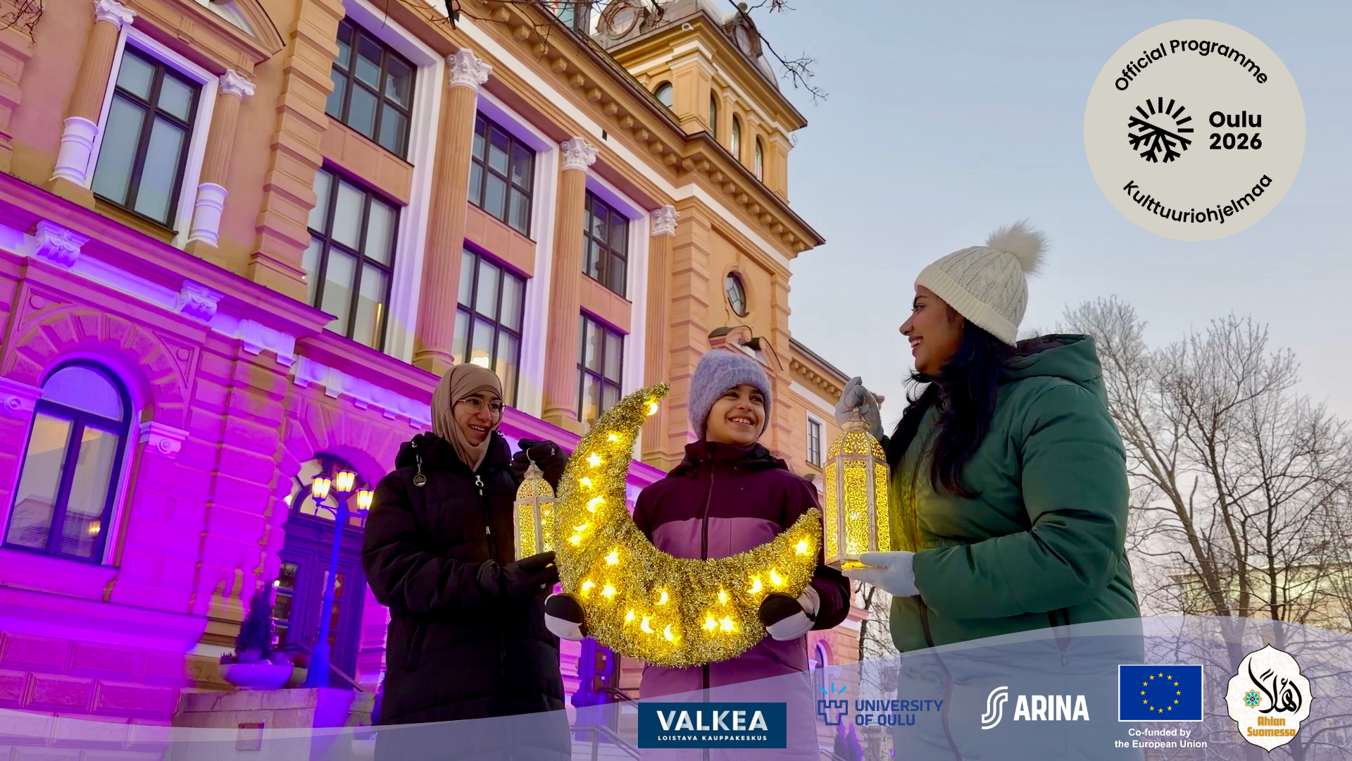 Three girls holding lanterns and a cresent as Ramadan symbols in front of Oulu city hall smiling to each other. The photo is part of the program promo.