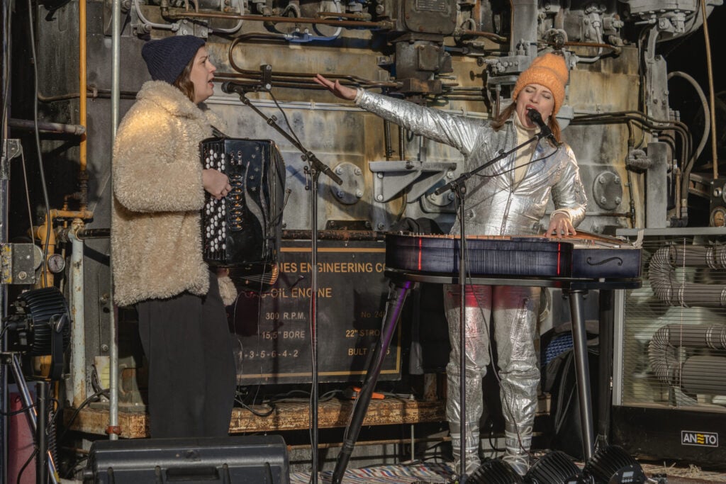 Ida Elina ( kantele) and Teija Niku ( accordion) performing in front of the Rathbun-Jones Engine in The Cultural Heritage Center in Oulainen. Photo by Minna Kesti.