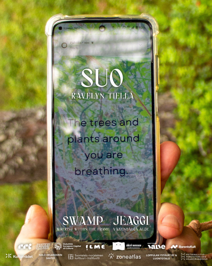 Swamp - Walking Within the Frame. In the photo, a close-up shot of a smartphone displaying the text "Trees and plants around you are breathing". Photo: Stein Valkoinen.