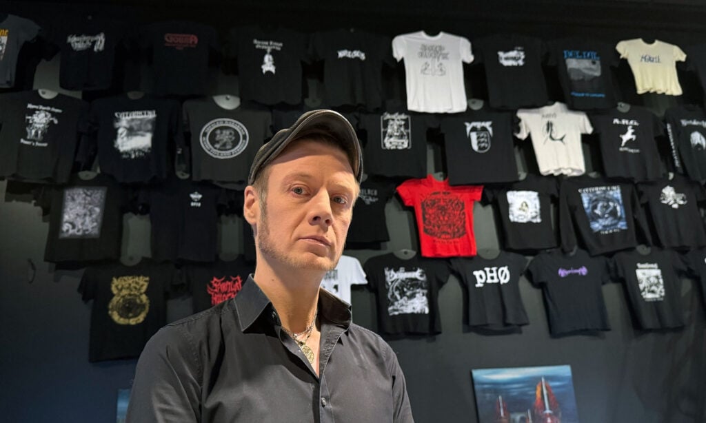 Tutkija Tuomas Niemelä Metallikauden Äänekäs Kansa -paitaseinän äärellä. Näyttelyyn saatiin bändipaitoja enemmän kuin seinälle mahtui.